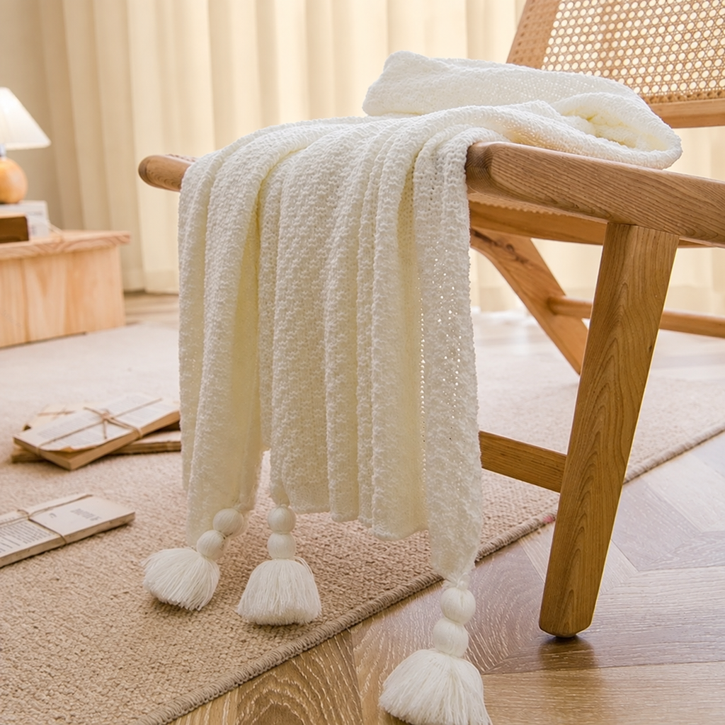 Plaid blanc à maille légère et pompons sur un fauteuil en bois