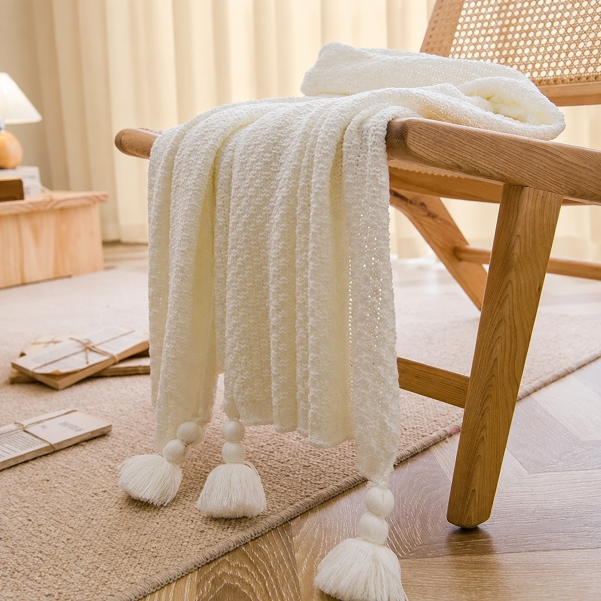 Plaid blanc à maille légère et pompons sur un fauteuil en bois