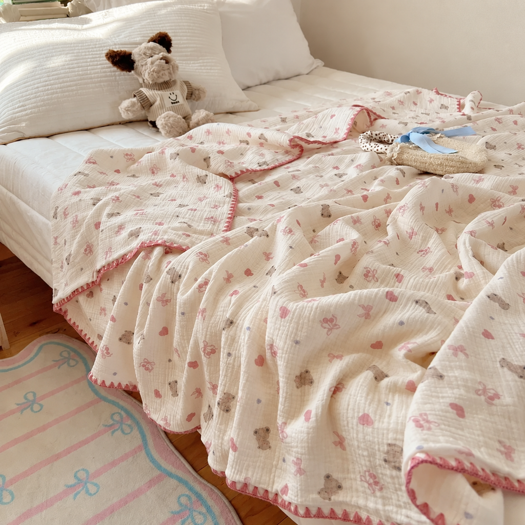 Plaid écru à motifs oursons et cœurs roses sur un lit près d’un mur beige