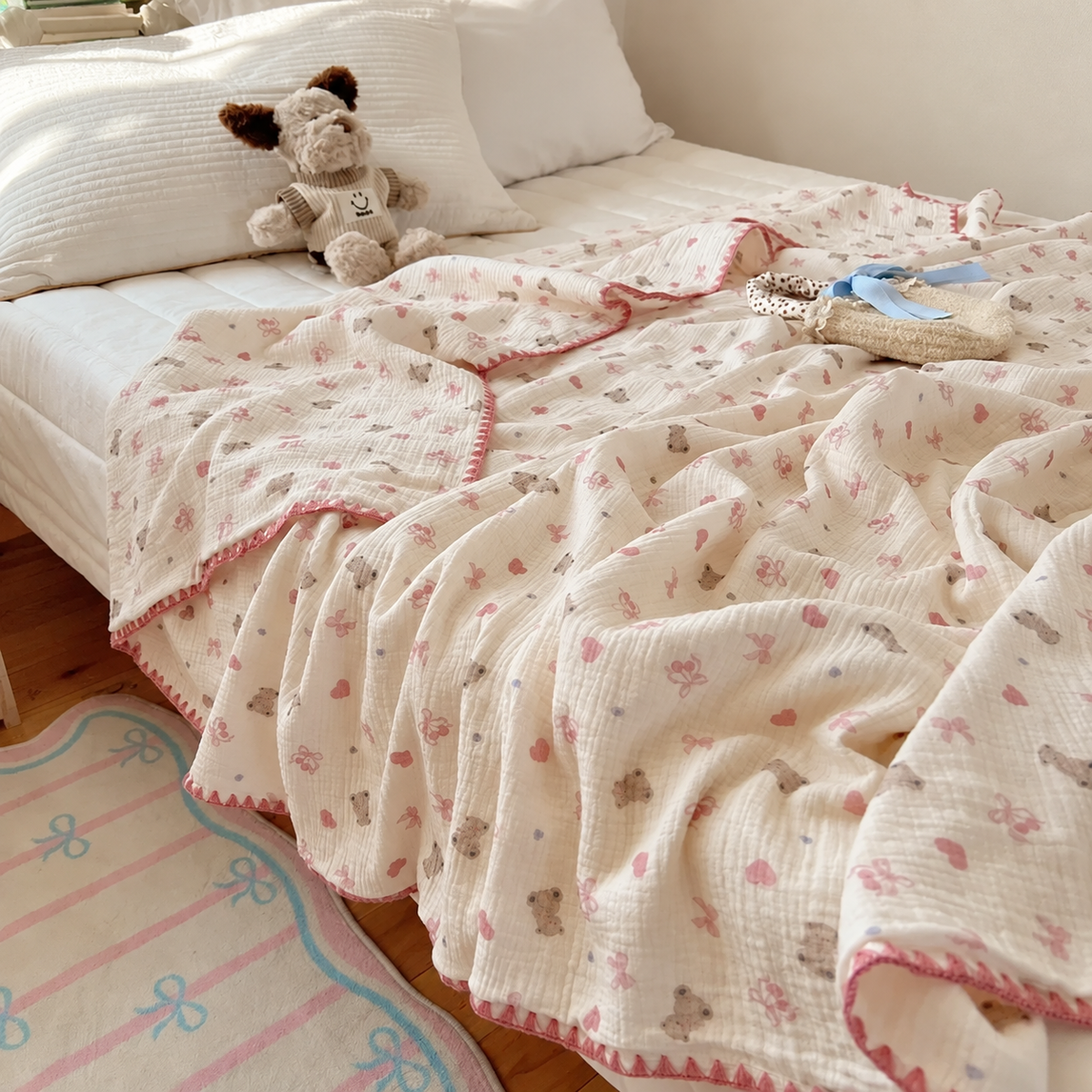 Plaid écru à motifs oursons et cœurs roses sur un lit près d’un mur beige