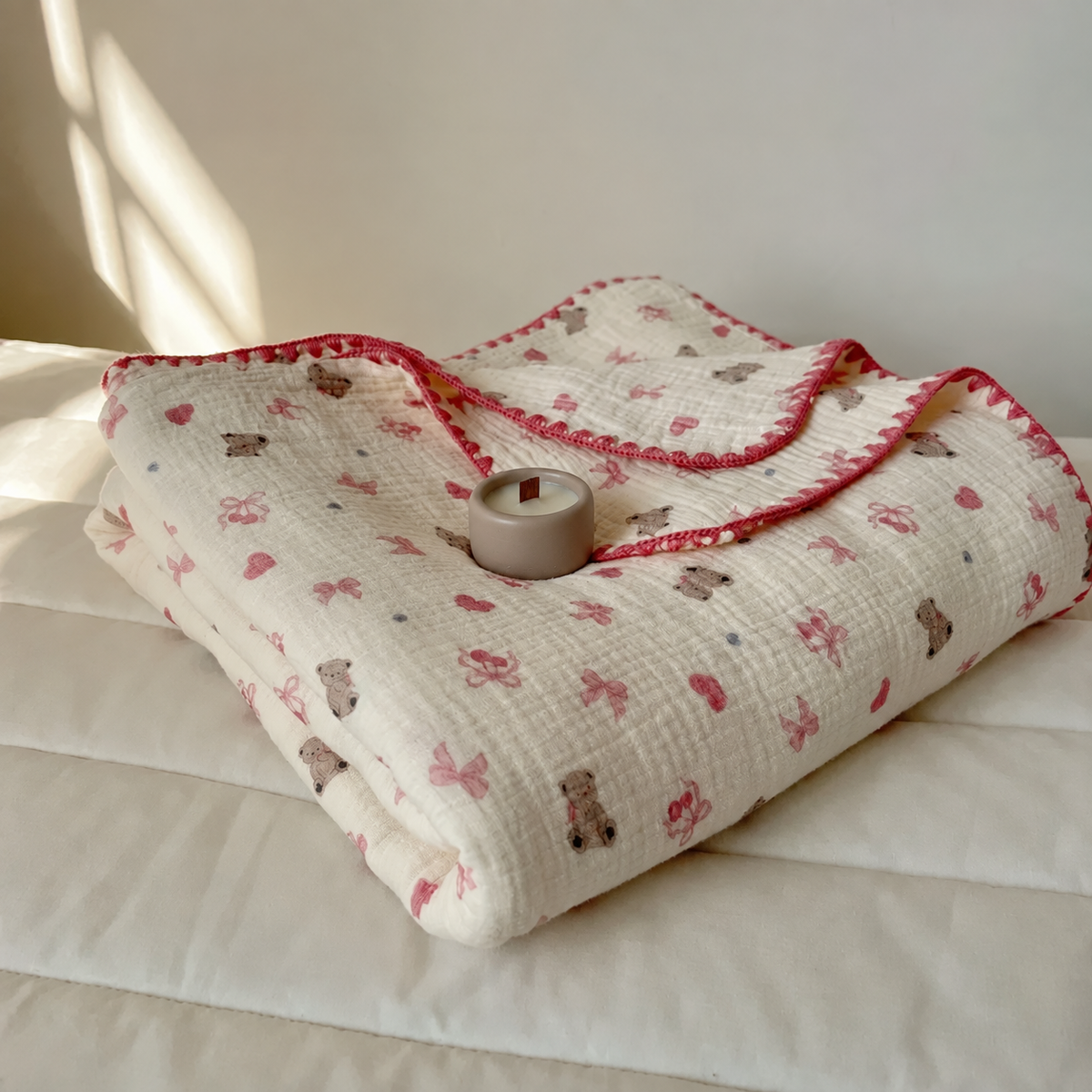 Plaid en coton à motifs oursons plié avec un petit pot taupe