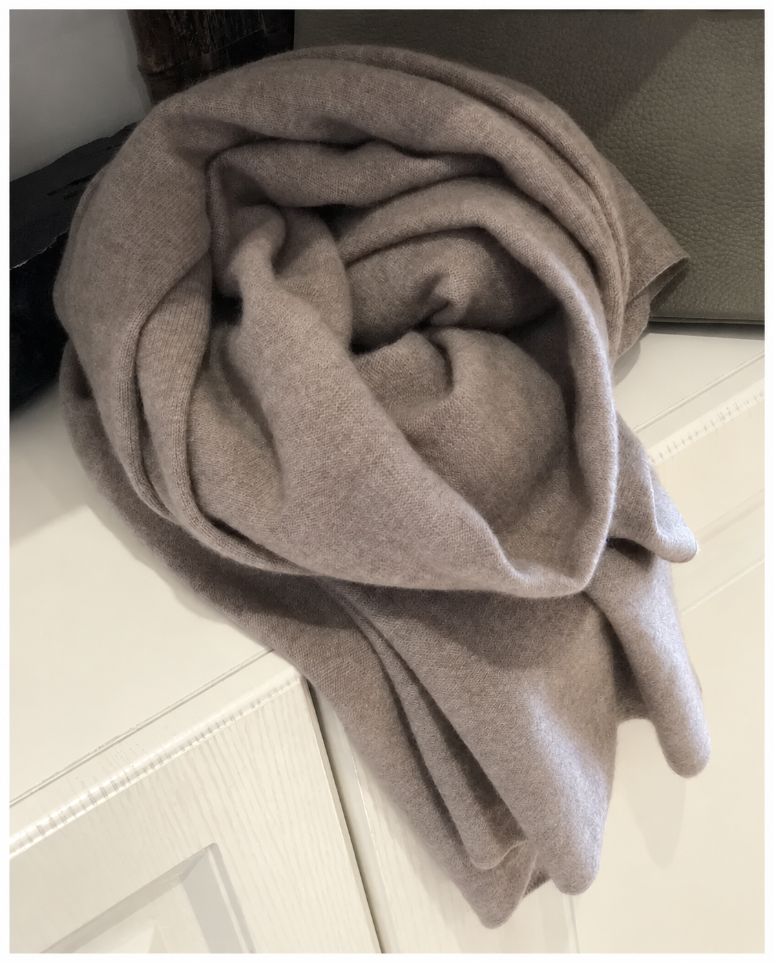 Écharpe taupe enroulée sur un meuble ivoire
