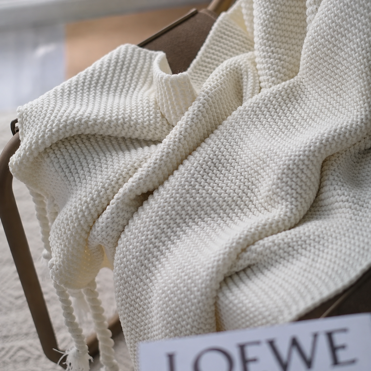 Détail du plaid blanc tricoté à franges torsadées sur un fauteuil