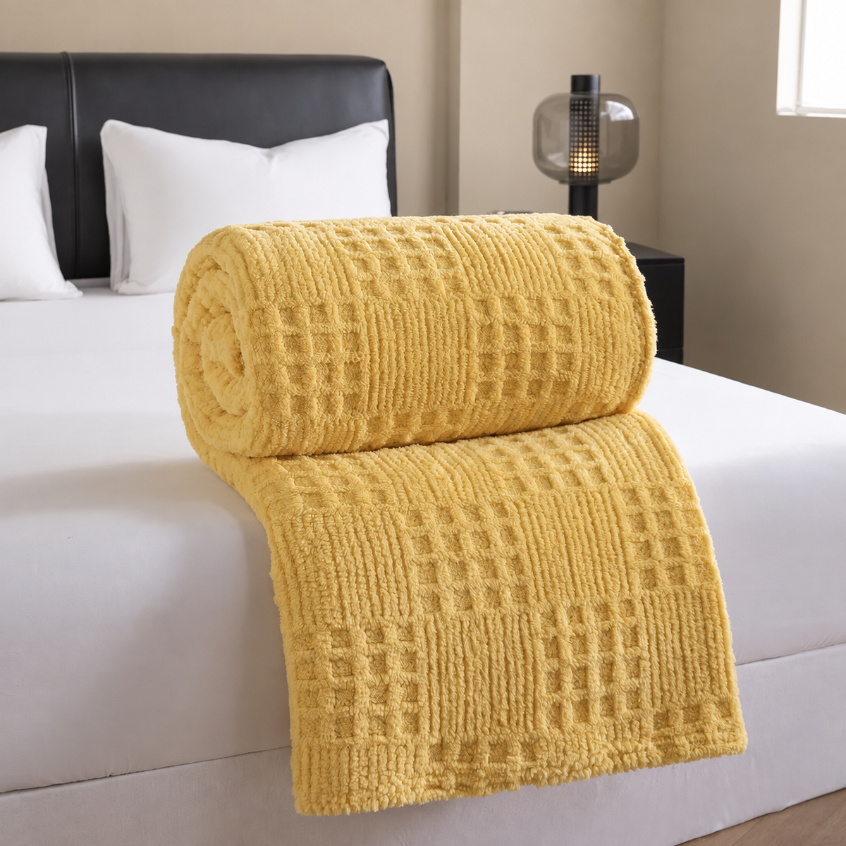 Plaid jaune jacquard gaufré roulé sur un lit blanc dans une chambre beige