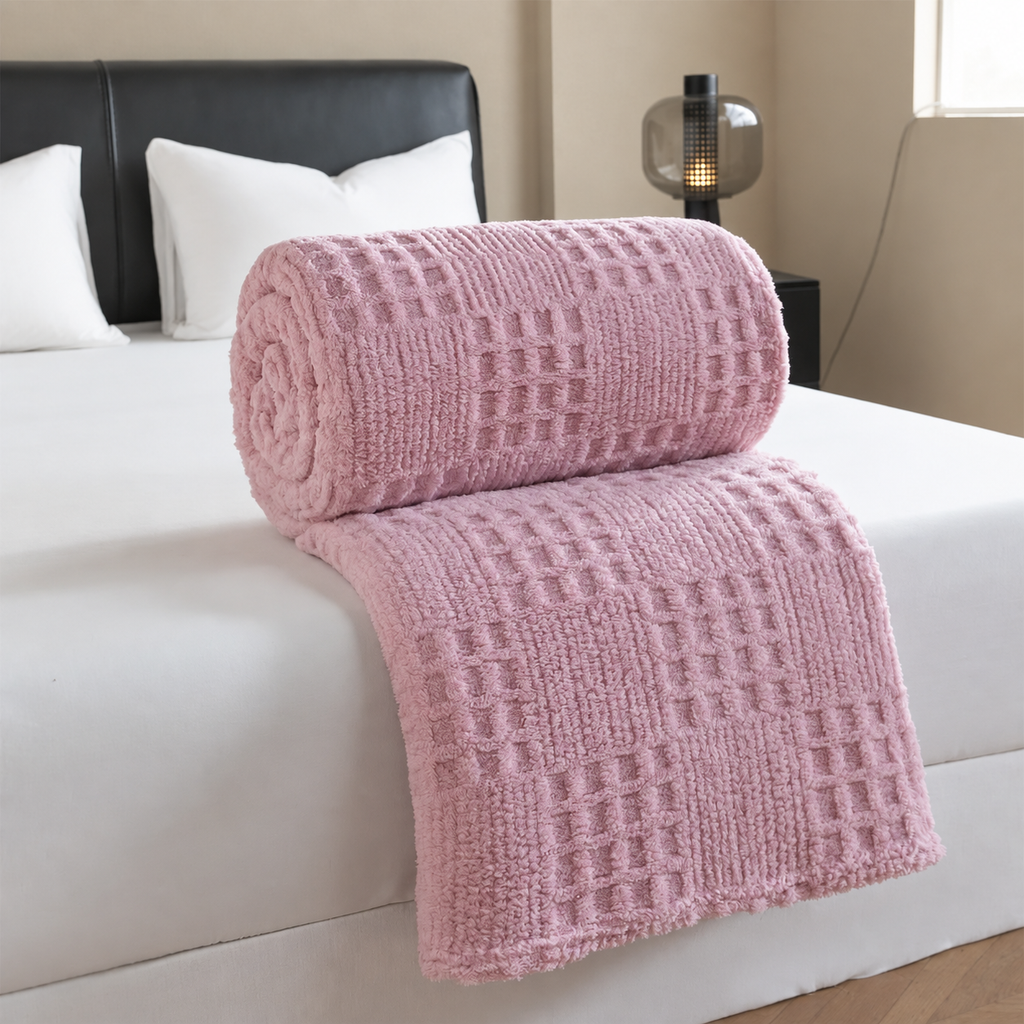 Plaid rose jacquard gaufré roulé sur un lit blanc dans une chambre beige