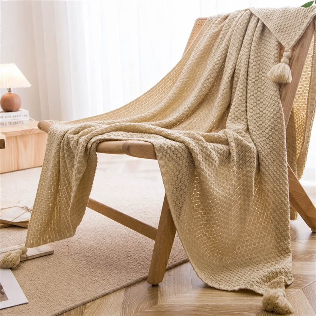 Plaid beige à maille gaufrée et pompons sur un fauteuil en bois
