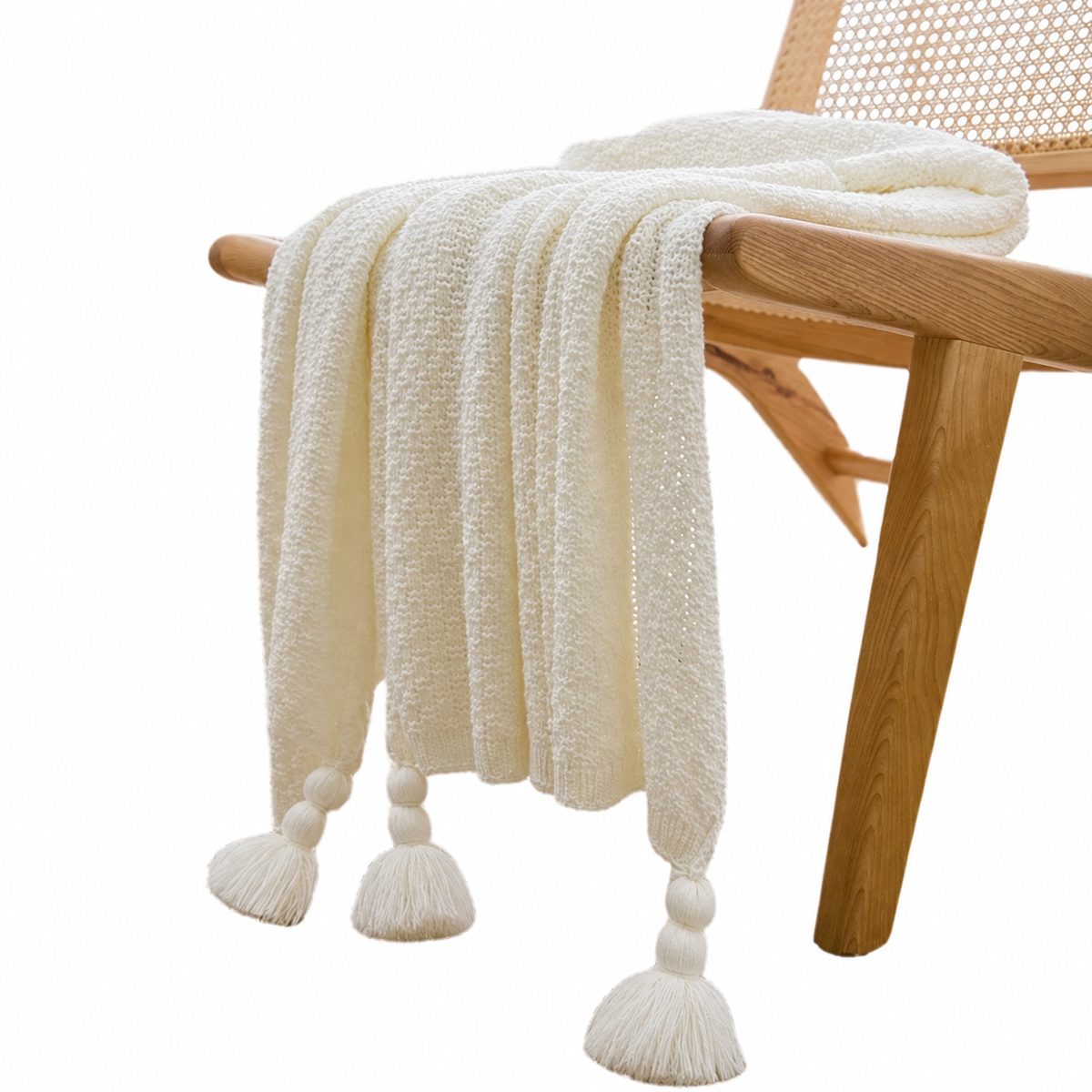 Plaid blanc à maille texturée et pompons drapé sur une chaise, fond blanc